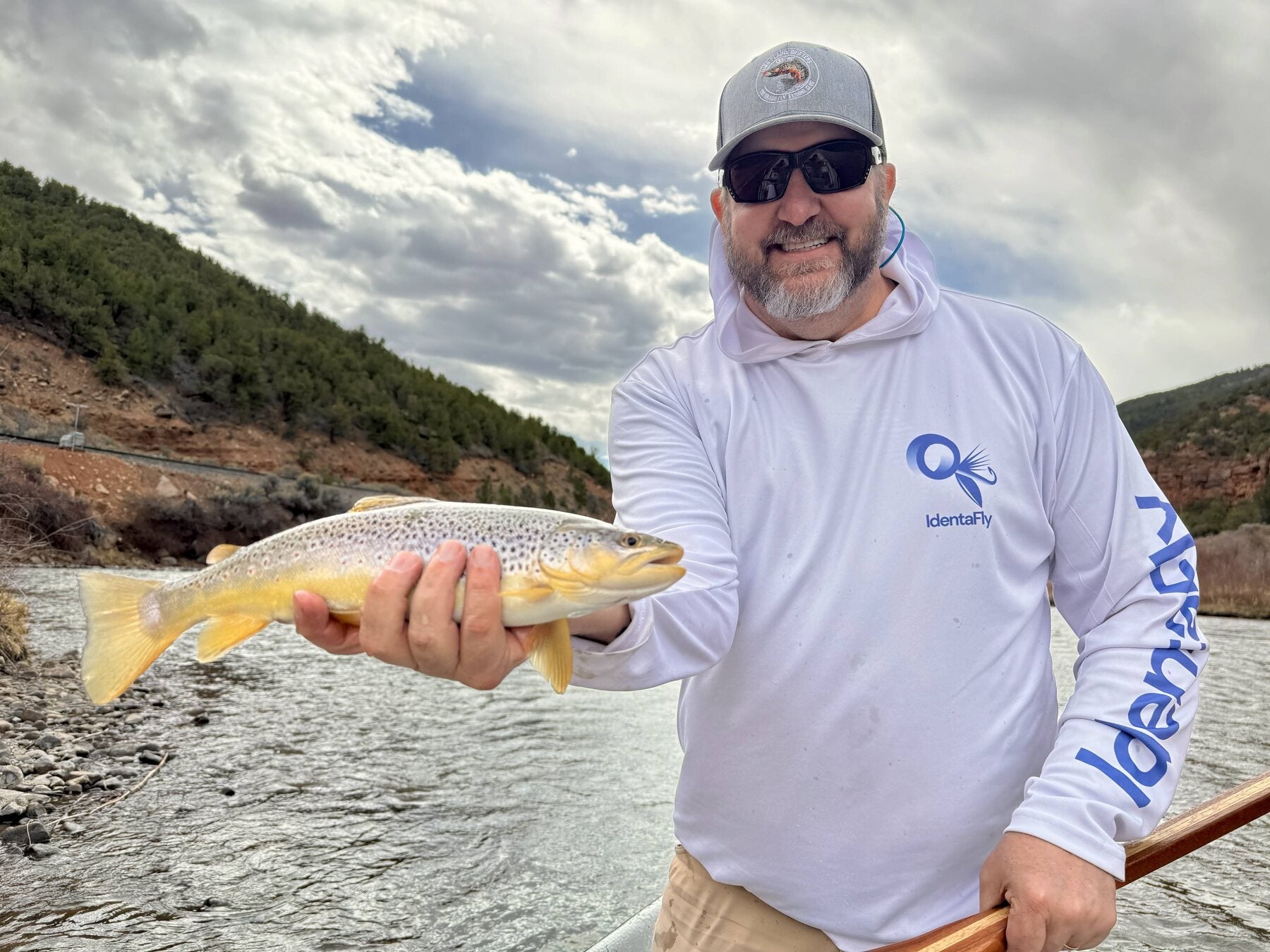 High Plains Drifters member holding a brown trout beside a Colorado river